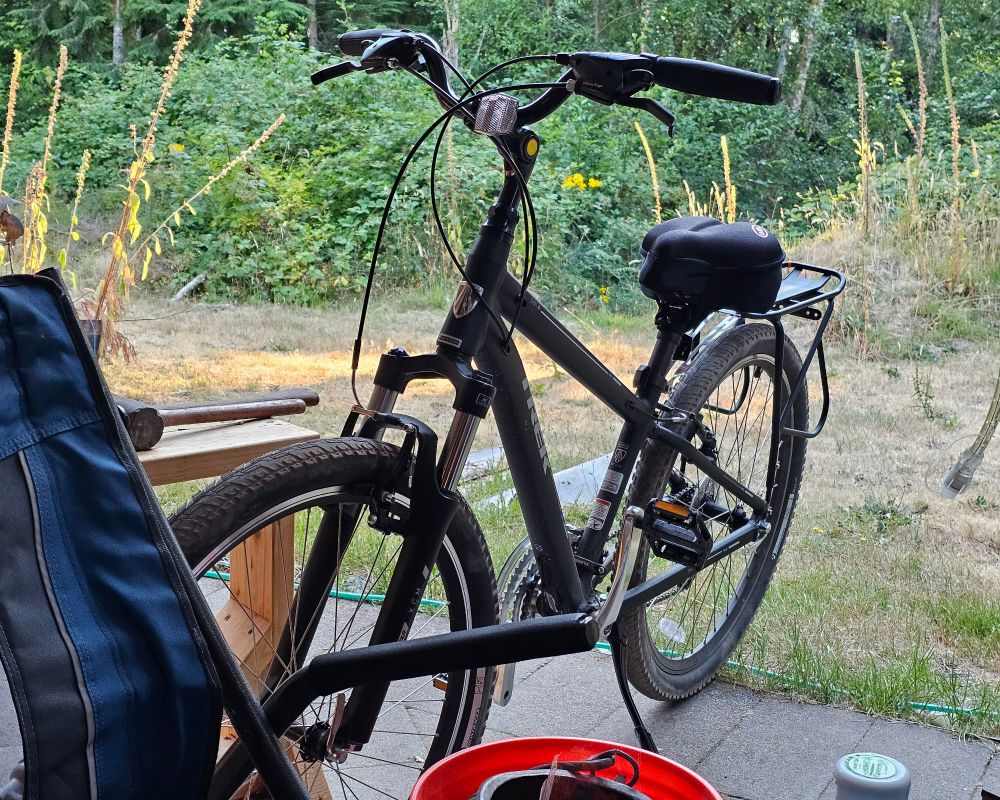 Slightly dusty black bike, patio accumulations, and a summer evening.