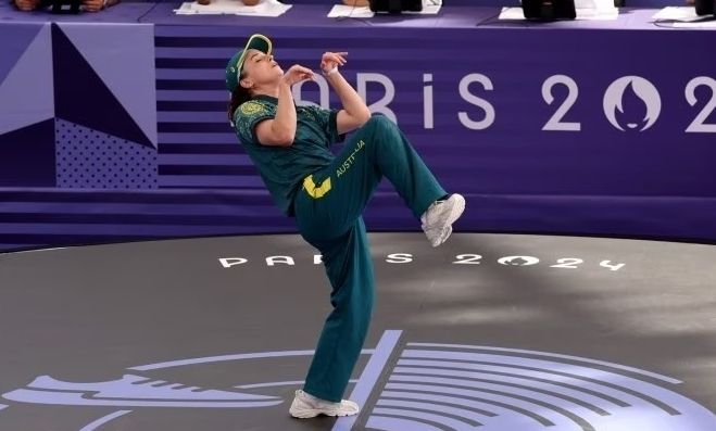 Die australische Breakdance-Athletin Rachel Gunn bei den Olympischen Spielen. Sie hat ein Bein angewinkelt weit nach oben gezogen, ihr Oberkörper neigt sich im Bogen hinten und ihre Hände sind nach oben vor dem Oberkörper gezogen. Die Pose wirkt wie ein schleichender Dieb in Trickfilmen.