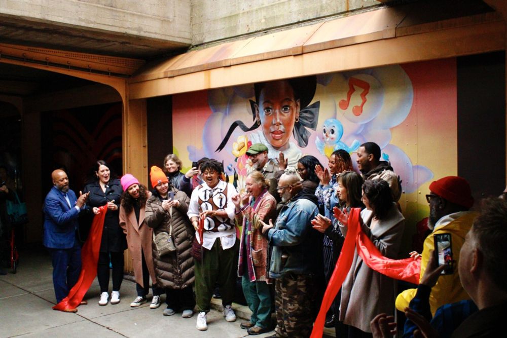 The artists whose works chosen for display along 53rd and 55th street viaducts in Hyde Park celebrate the ribbon-cutting of the refreshed “viaduct galleries” during an outdoor ceremony on May 22, 2025. In the background is Kayla Mahaffey’s “Head in the Clouds.” Credit: Maxwell Evans/Block Club Chicago
