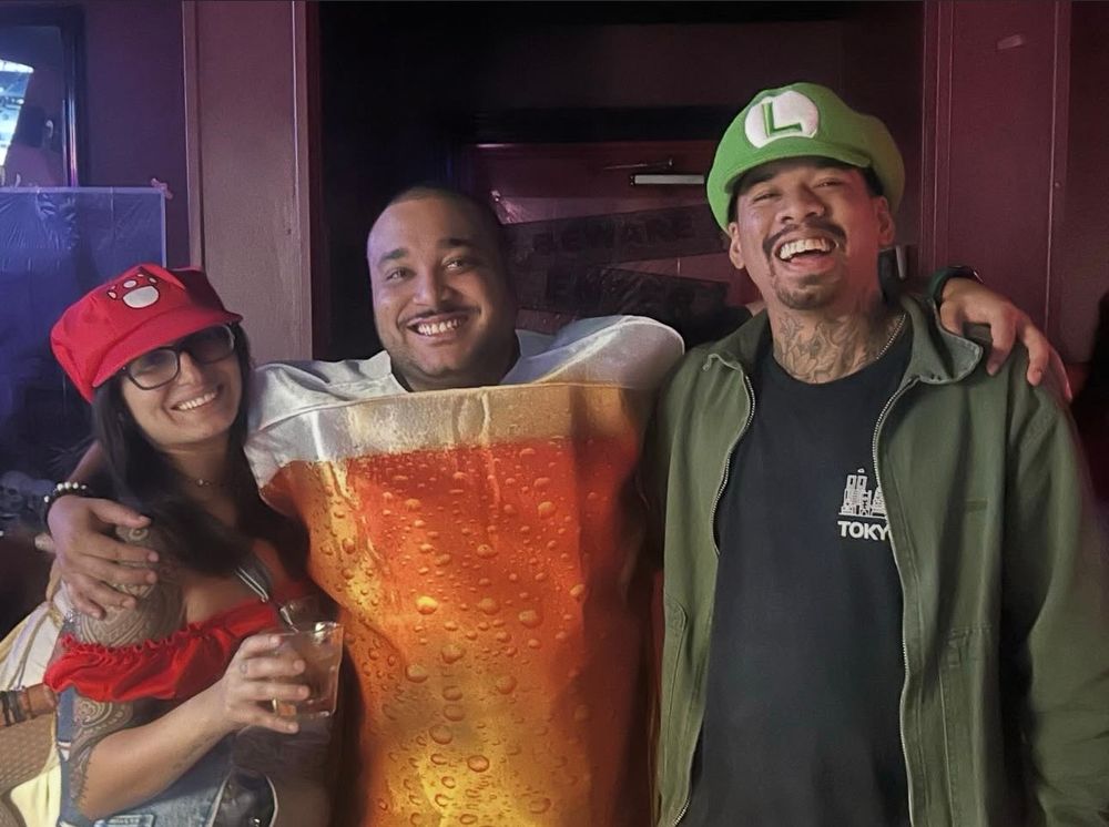 A photo of @MissyMelliott, her boyfriend, and a friend. She is dressed as Mario, her boyfriend is Luigi, and their friend is a glass of beer