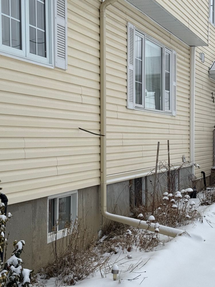 A house with pale yellow siding that has large twig sticking out of it at a perpendicular angle. The twig impaled the siding in a wind storm

