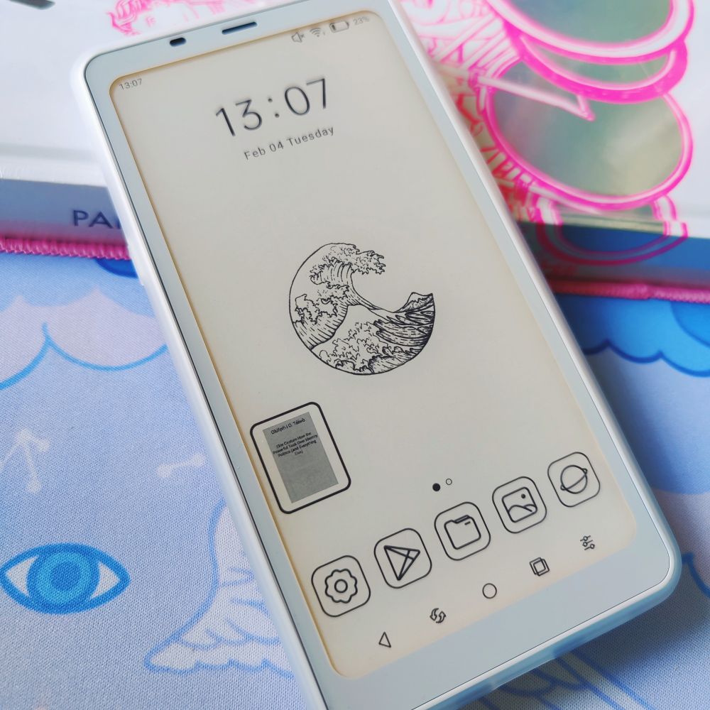 Front of a phone sized e-reader with a black and white e-ink screen and a standard Android OS home page with a clock on top and app icons in the bottom drawer