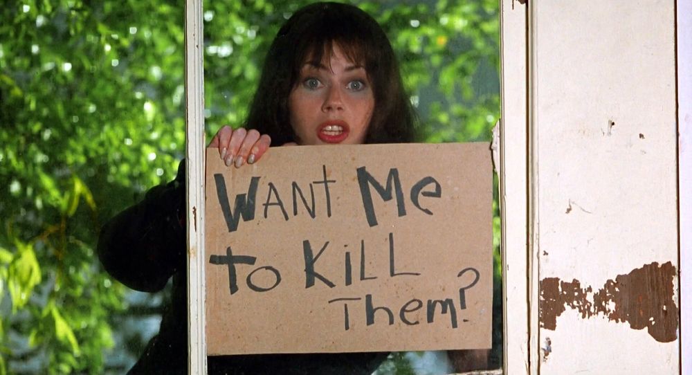 Fairuza Balk in Waterboy holding up a sign outside a window that says, "Want me to kill them?"