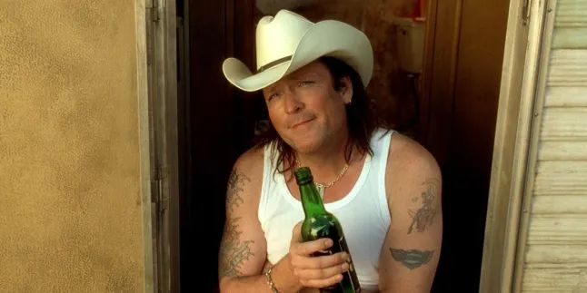 Michael Madsen, wearing a cowboy hat and holding a bottle of booze