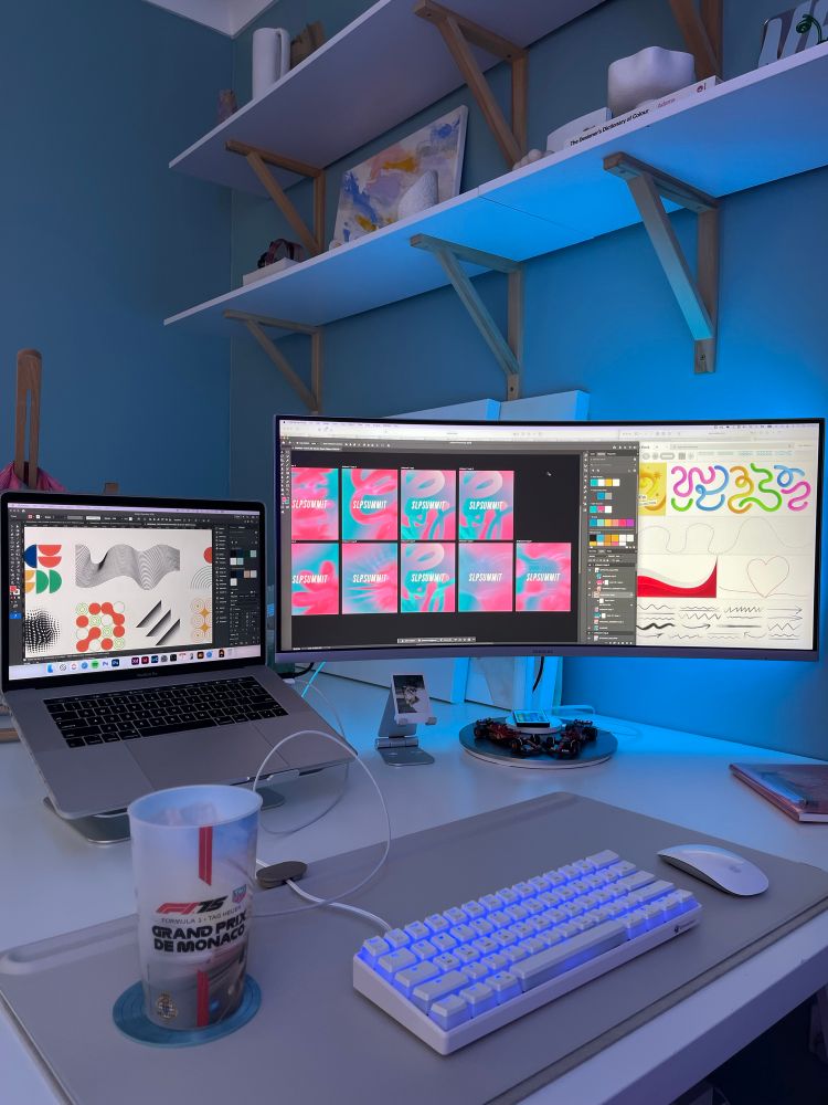 A photo of my desk showing illustrator open with shape graphics inside, adobe stock open, and photoshop open with a whole bunch of versions of gradients and overlays with blur applied 