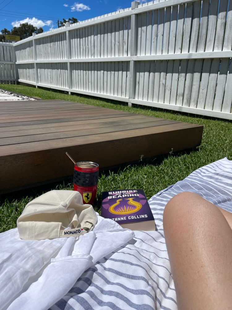 A white linen shirt, cap from the monaco oceanographic museum, sunrise on the reaping book and a Ferrari cup with an iced coffee in on a cotton towel on the lawn