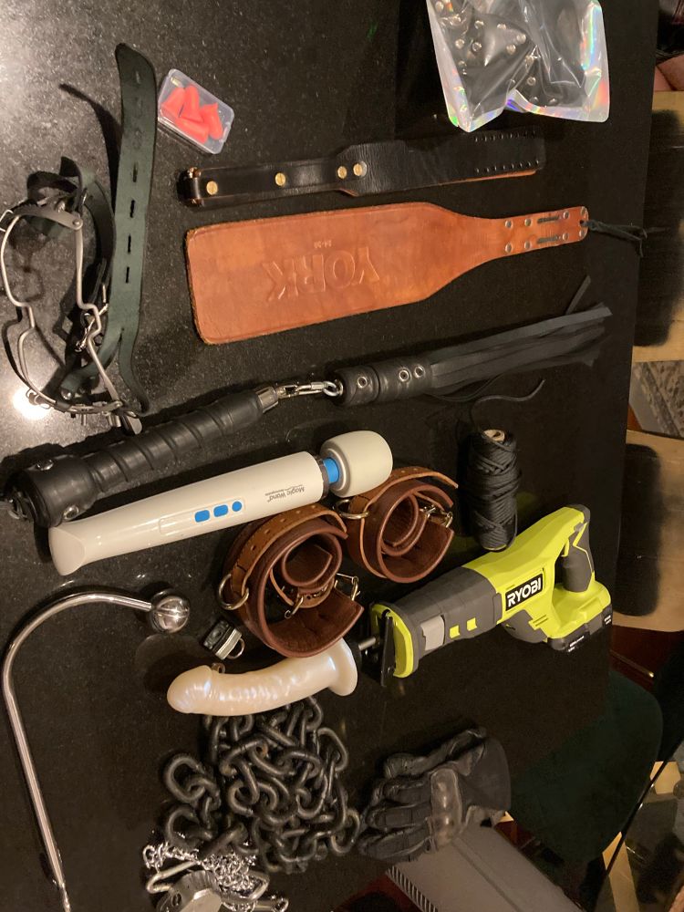 On the table there’s a saws-all with a dodo attached, some chain and leather cuffs, some floggers, a hitachi magic wand, and gags.