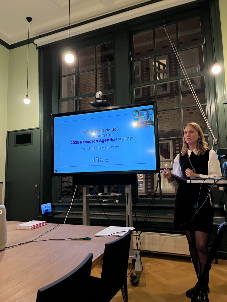 Lab manager Sara Spaargaren is standing next to a screen presenting the 2025 research agenda of the AI Media and Democracy Lab
