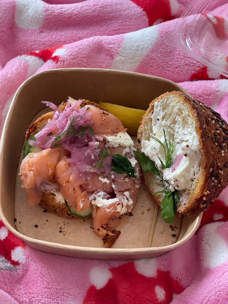 A square dish holds two halves of an open face smoked salmon sandwich 