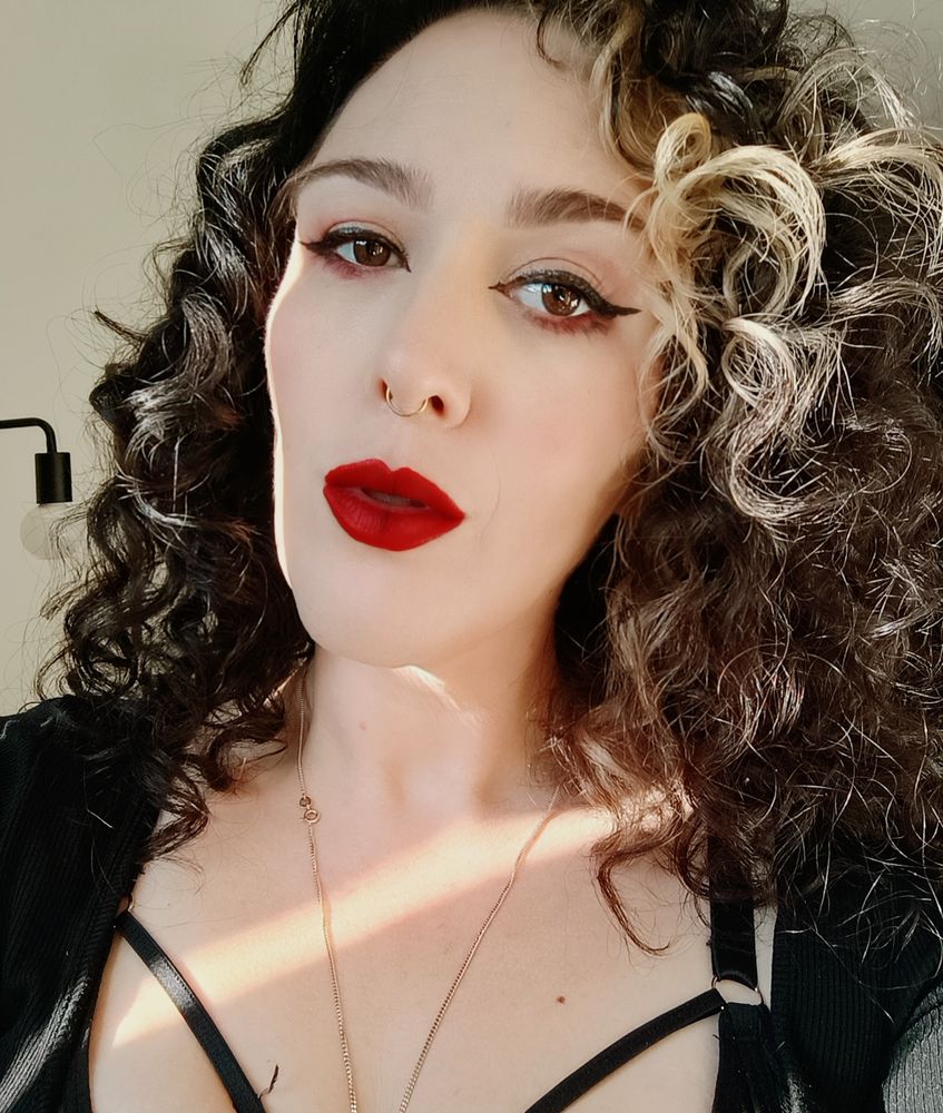 woman with black hair, red lips, red eyeshadow, and black eyeliner staring at the camera