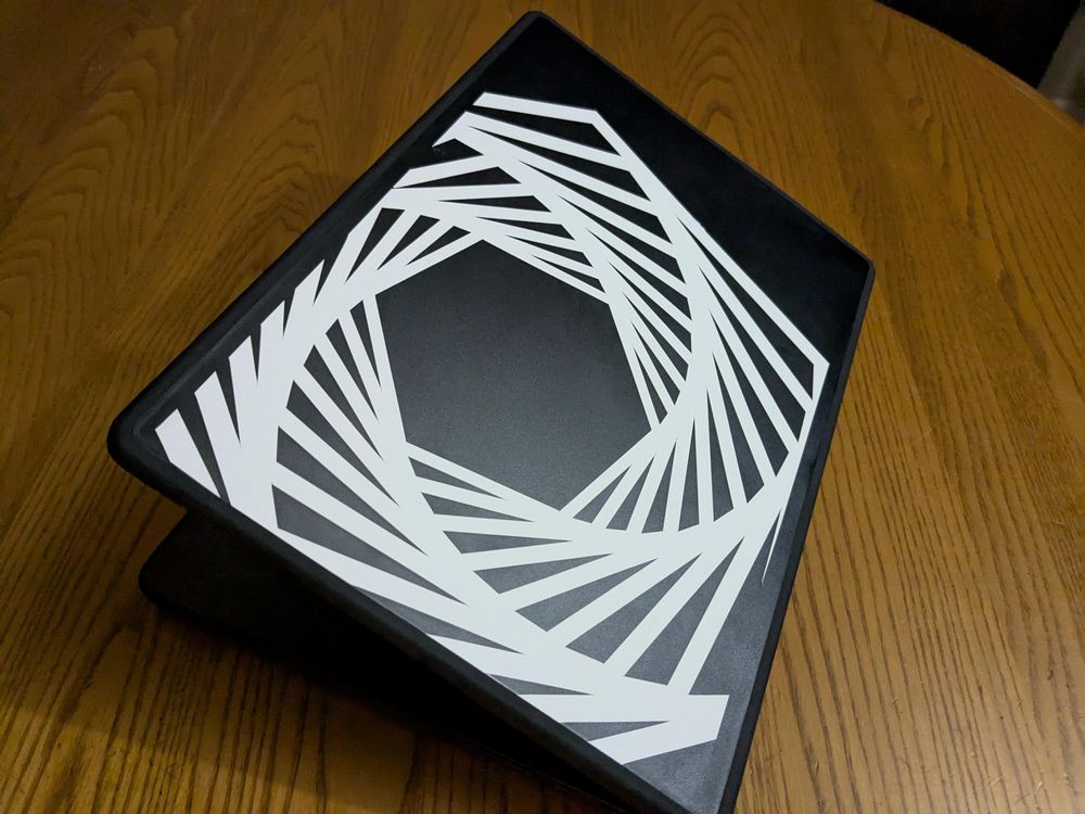 A MacBook with a dark gray case on it. Covering most of the case is a single white vinyl sticker, a series of finely-cut spiraling hexagons nested one inside the other.