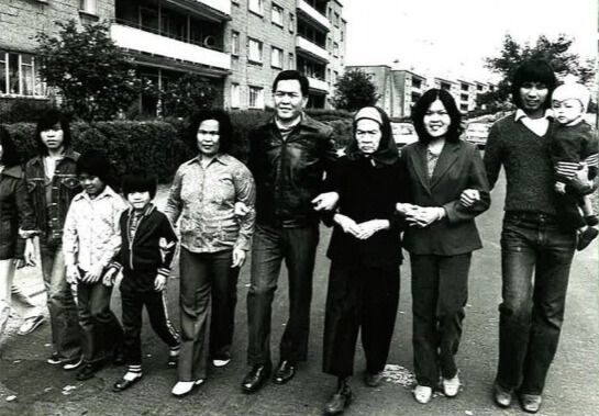 Black and white photograph of refugees from Vietnam who have settled in Scotland linking arms in a residential street in front of blocks of flats