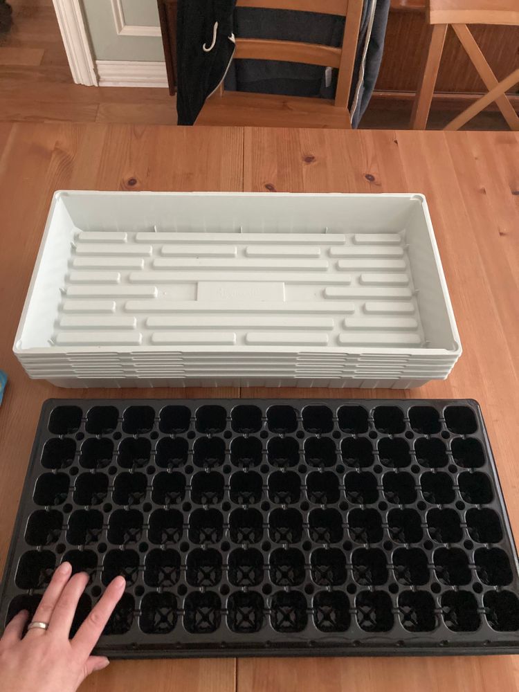 A stack of seed starters and a stack of water trays for the seed starters, with a wee hand for scale.
