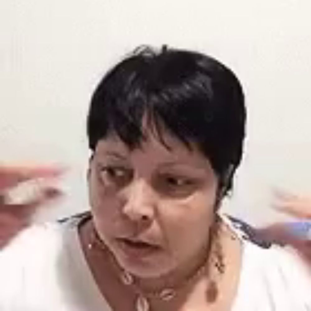 a woman with short black hair is wearing a white shirt and a necklace and making a funny face .