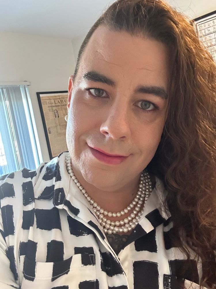 ML is wearing a black and white dress and a pearl necklace. Her makeup is done and they’re looking into the camera