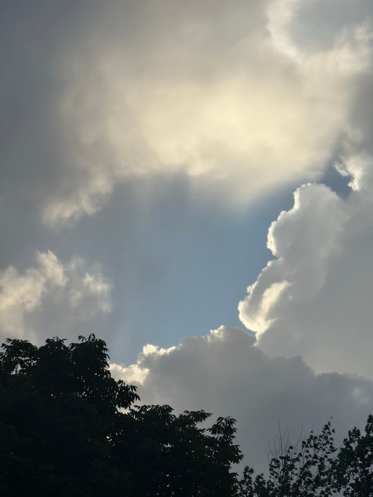 A photo of storm clouds during a spring evening, with the setting sun shining from behind the dark clouds.
