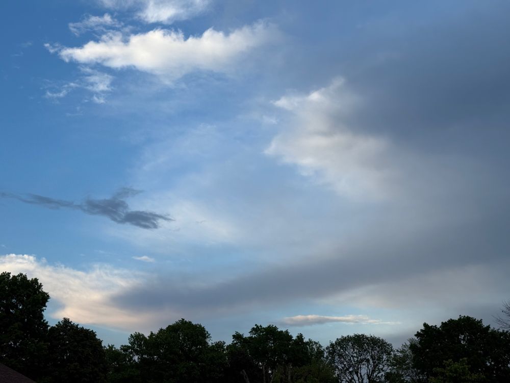 A photo of the sky after a spring storm, with dark clouds on the right, blue sky on the left, and a line of trees beneath.