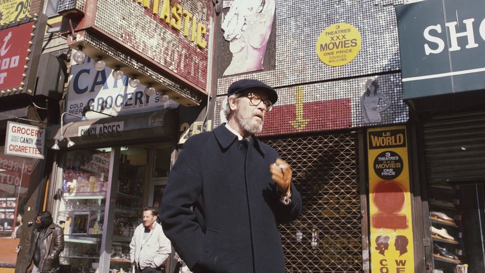 The late author Elmore Leonard pictured wearing his trademark newsboy cap in a gritty urban environment, perhaps New York City's Time Square.