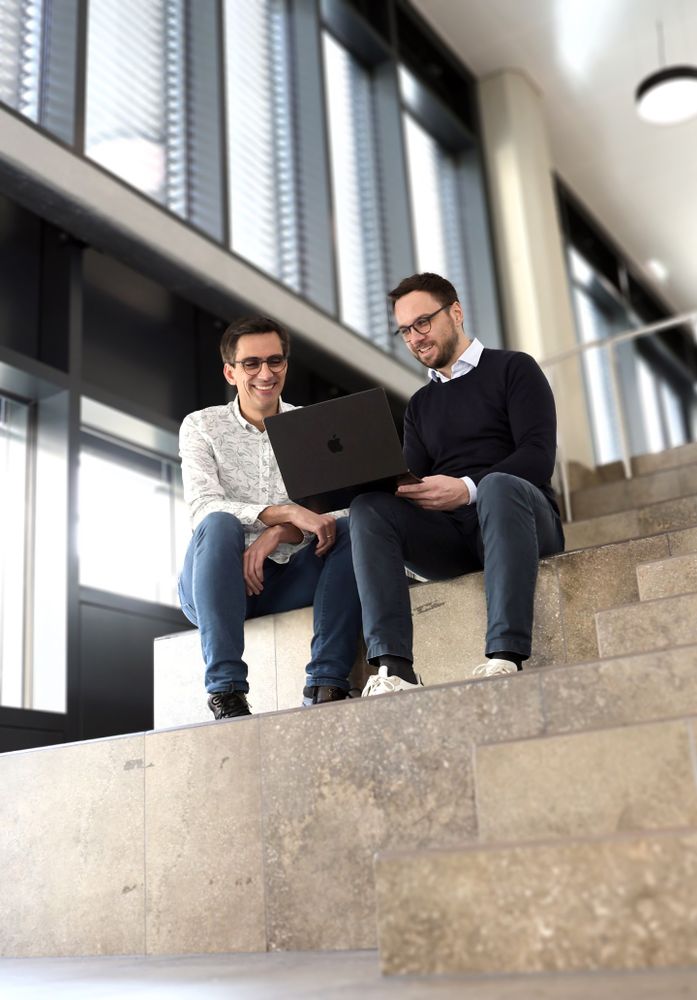 Zwei Männer sitzen auf Treppen und schauen auf einen Laptop.