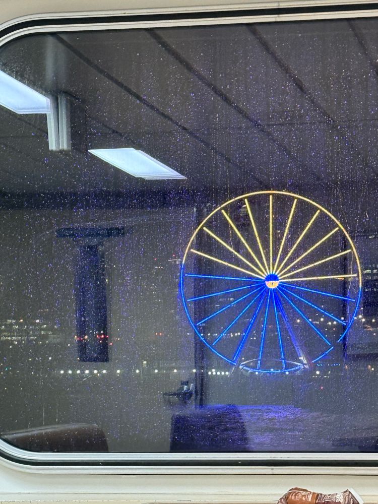 Seattle Ferris wheel, lit up in yellow and blue, through a rainy ferry window.  