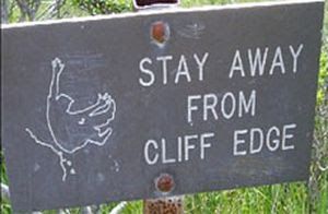 A sign reading "Stay away from cliff edge" with an outline of a body falling off the edge of a cliff.