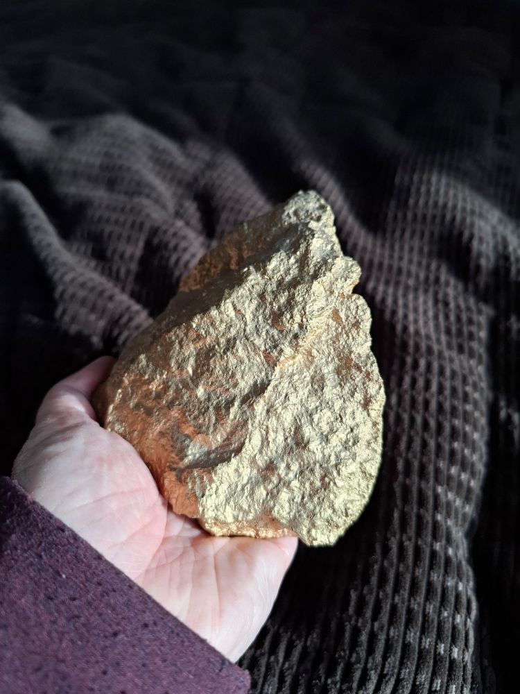 A hand holding a pointy rock that has been painted gold.  It was awarded to the recipient because they did a damned good job
