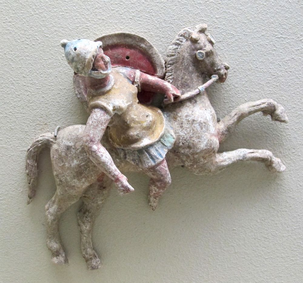 Terracotta of an Amazon, mounted on a horse, wearing a cuirass molded to show female anatomy, wearing a knobbed Montefortino helmet with holes where plumes could be inserted.