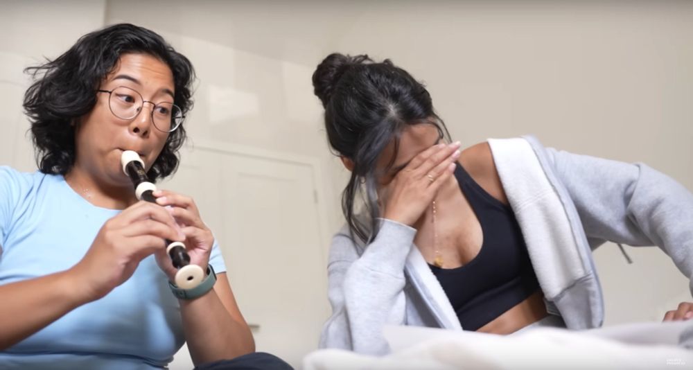 someone is playing the flute on the left, and the person next to her is looking exasperated, their hand over their face