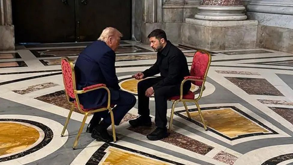 In the vast grandeur of St Peter's Basilica, President Trump and President Zelensky are seated on two small chairs, very close together. Zelensky is talking intensely. Trump's back is to the camera, but we can presume he is struggling to understand.