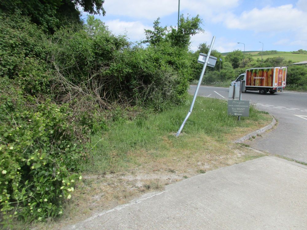 Rear view of crash-damaged post with van in the background.