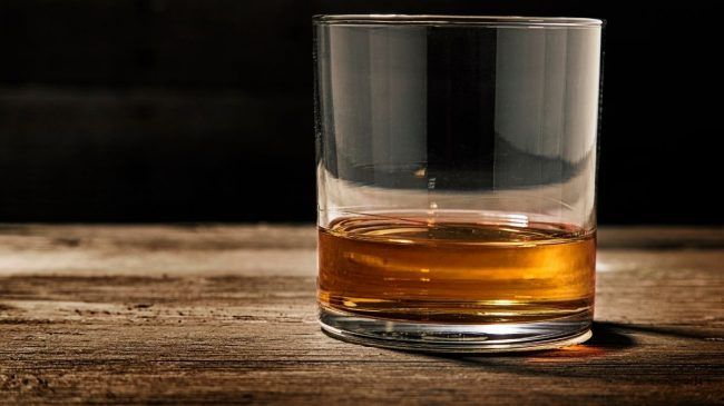 a glass of bourbon on a wooden surface
