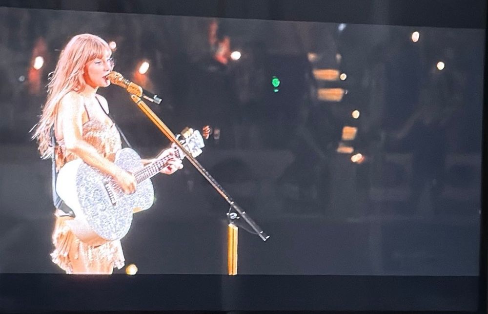 Taylor Swift wearing gold playing a silver guitar