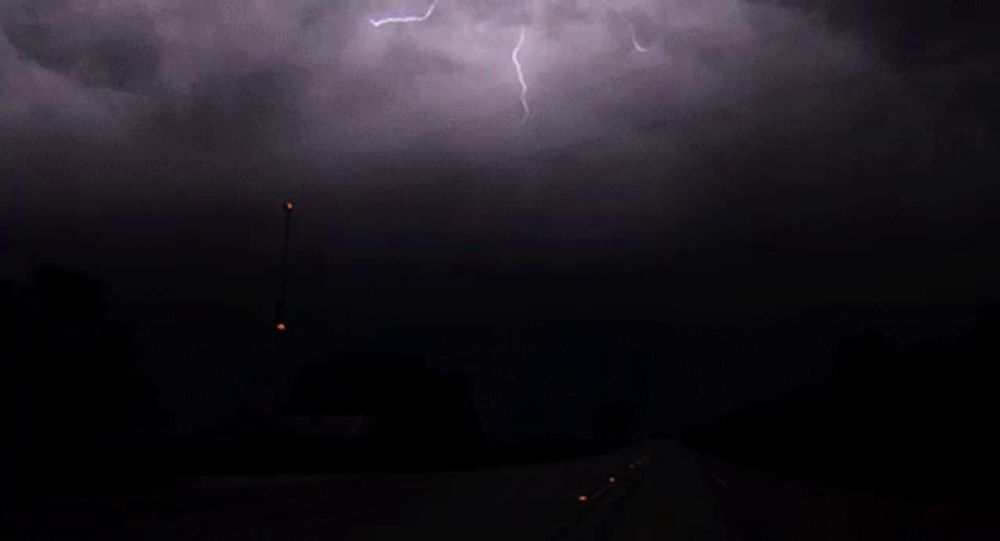 lightning strikes across a dark sky over a road