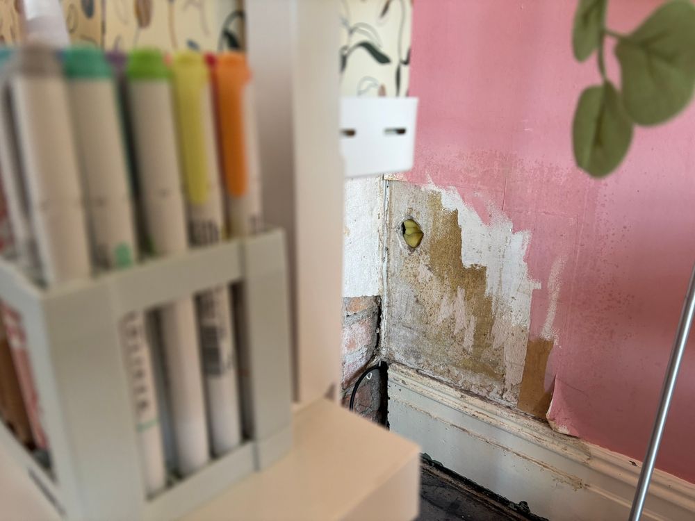 Foreground: highlighter pens and the corner of a desk. Background: the hole in the wall from a slightly different angle 