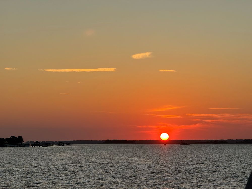 Sun going down over the ocean. The ocean is calm.  The sun still a whole ball but about to slip beneath the horizon. 