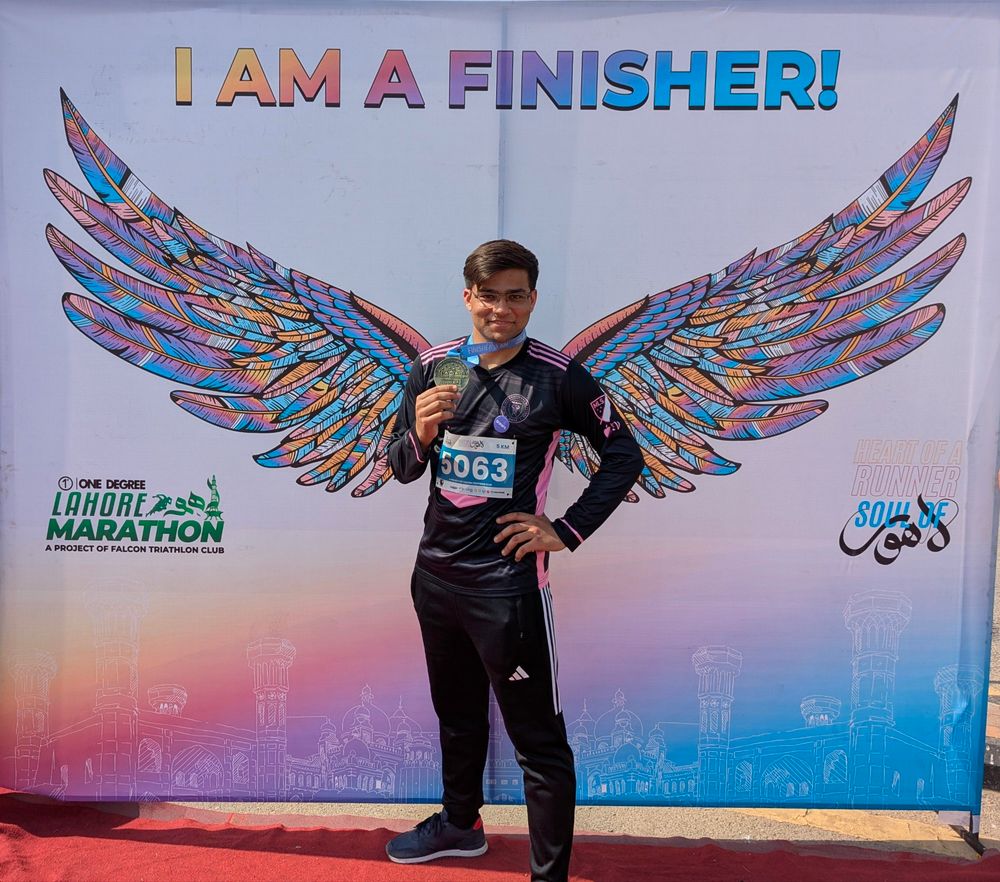 Me holding a medal for finishing a 5K run, in front of a banner saying "I am a finisher"