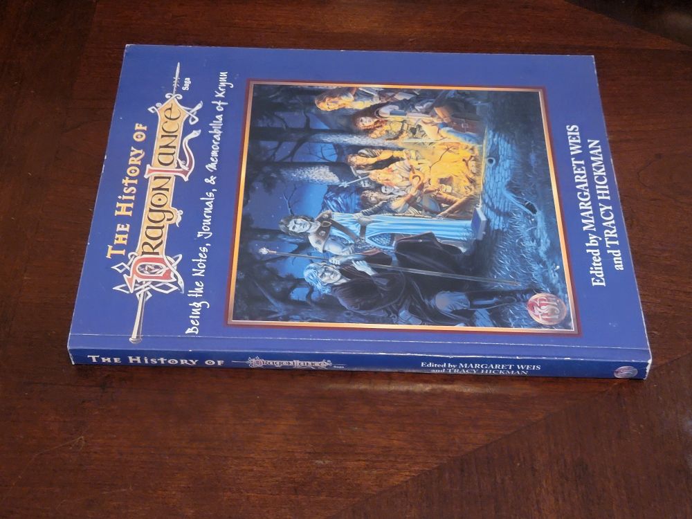 A side view of The History of Dragonlance book, showing the spine with very minor wear. The book is glossy, and sitting on a glossy wood table.