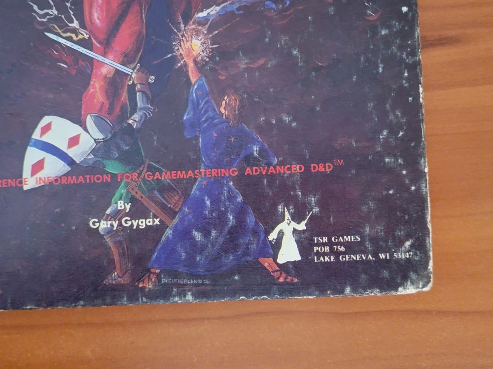 AD&D Dungeon Master's Guide - original 1979 printing. This is the bottom right corner of the cover, which still shows TSR Games with a Lake Geneva address. We can see a wizard from the cover, and a knight, both fighting the big demon (not really pictured in this closeup). These adventurers are hard to make out in the other images, but they fight nobly (with their backs to us, the audience) here in the corner.