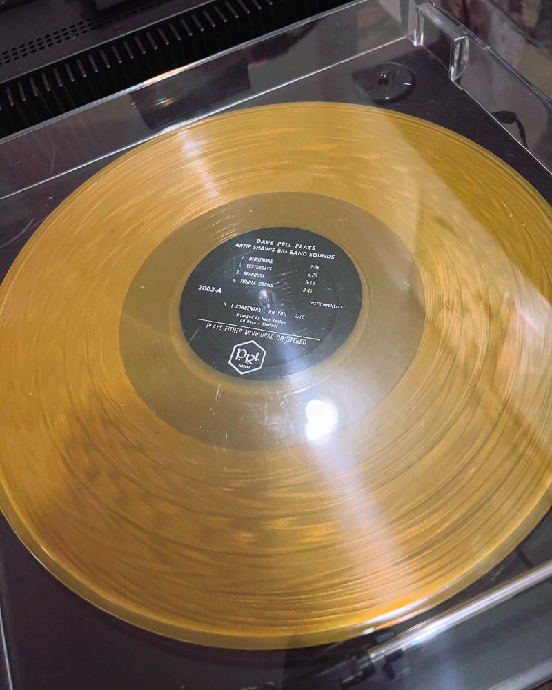 A translucent golden yellow vinyl LP record spins on a black turntable. The white print on the black label reads "DAVE PELL PLAYS ARTIE SHAW'S BIG BAND SOUNDS."