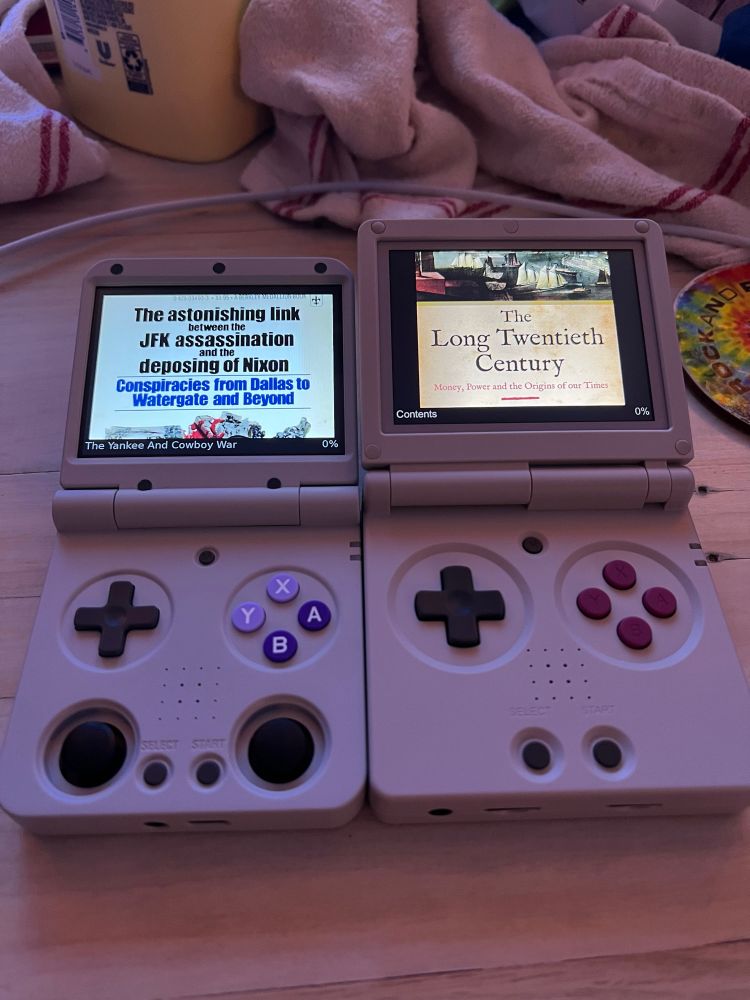 two handhelds that look like the gameboy advance sp’s displaying books