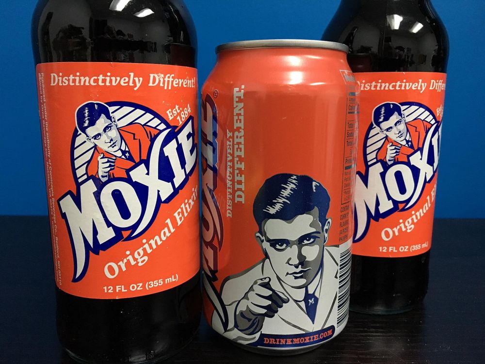 Two bottles and a can of Moxie. It has an orange label with "Moxie - Original Elixir" on it, with an old-fashioned black and white illustration of a man in a shit jacket (either white or orange, depending) who points to the viewer.