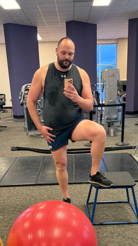 Man wearing a black sleeveless shirt and very short navy blue shorts with his thigh exposed. 