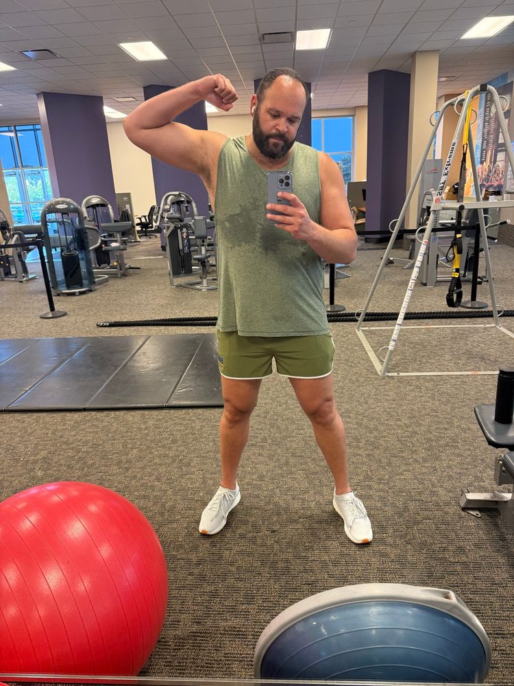 Man flexing bicep in olive green workout clothes. 