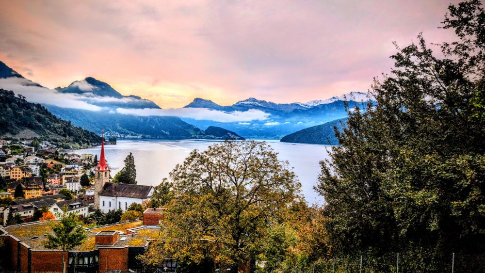 Mountains on the horizon stretching above the clouds, followed by a big lake and a pittoresque Swiss village in the foreground 