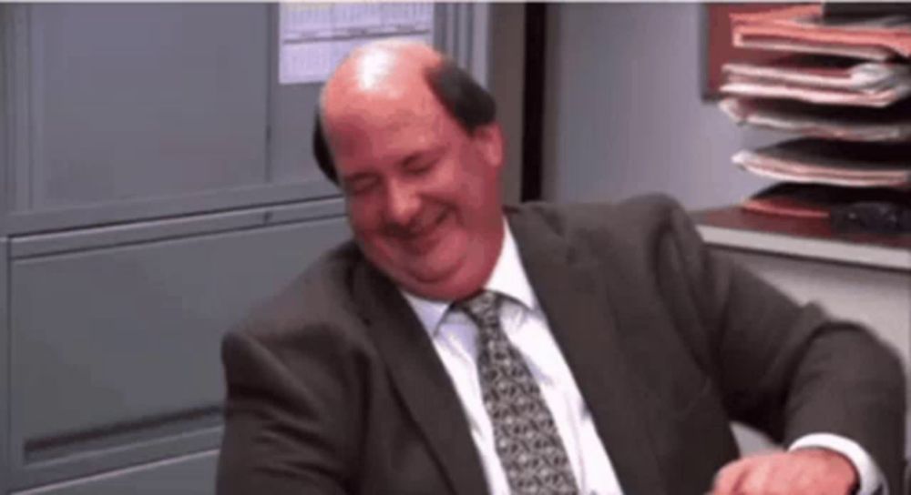 a bald man in a suit and tie is laughing while sitting in an office .