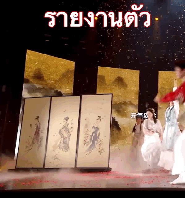 a group of people are dancing on a stage in front of a sign that says ' ราย งาน ตัว '