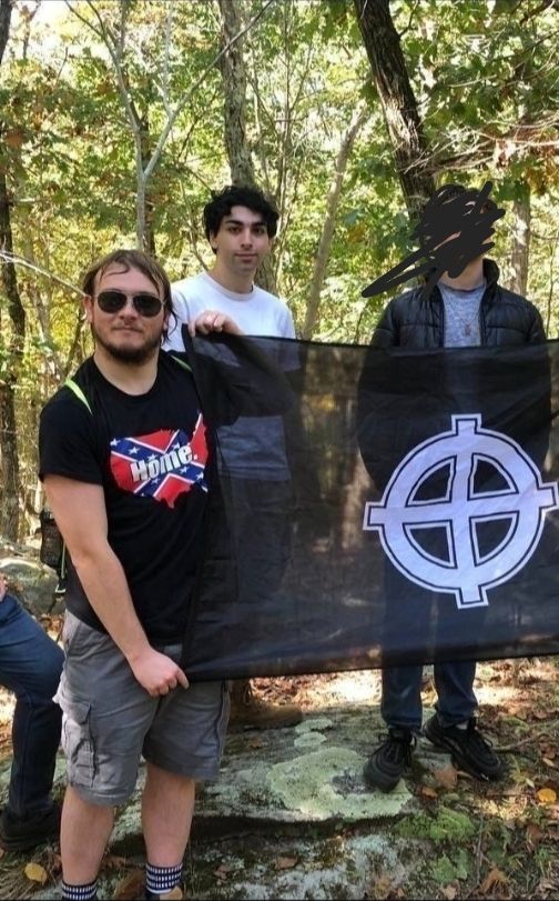 Sean Lemley wearing a confederate flag shirt while holding a white power flag, standing next to leader of his group Claudino Petrucelli, pictured in white tee shirt