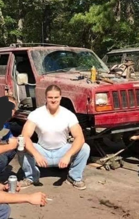 Samuel Kieffer Bray pictured squatting in front of a beat up red Jeep