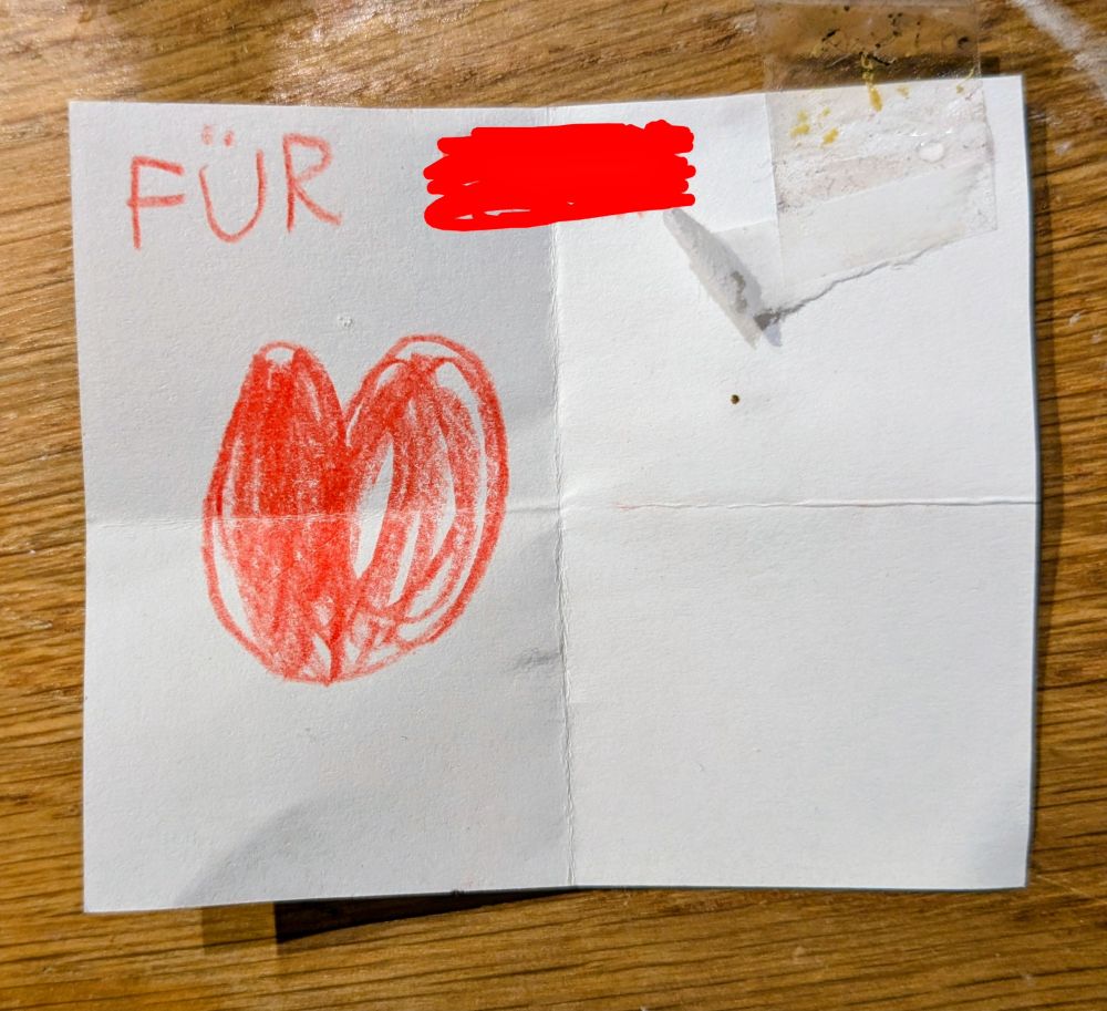 FÜR ... und ein kindgemaltes Herz in Rot auf einem kleinen Zettelchen mit einem kleinen Stück Klebeband.
