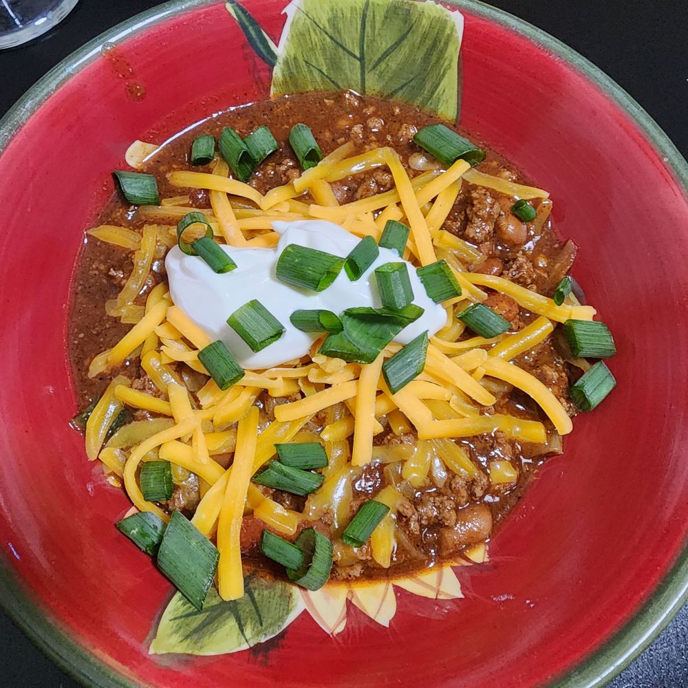 Bowl of chili topped with cheddar cheese, sour cream, and green onions I grew myself 